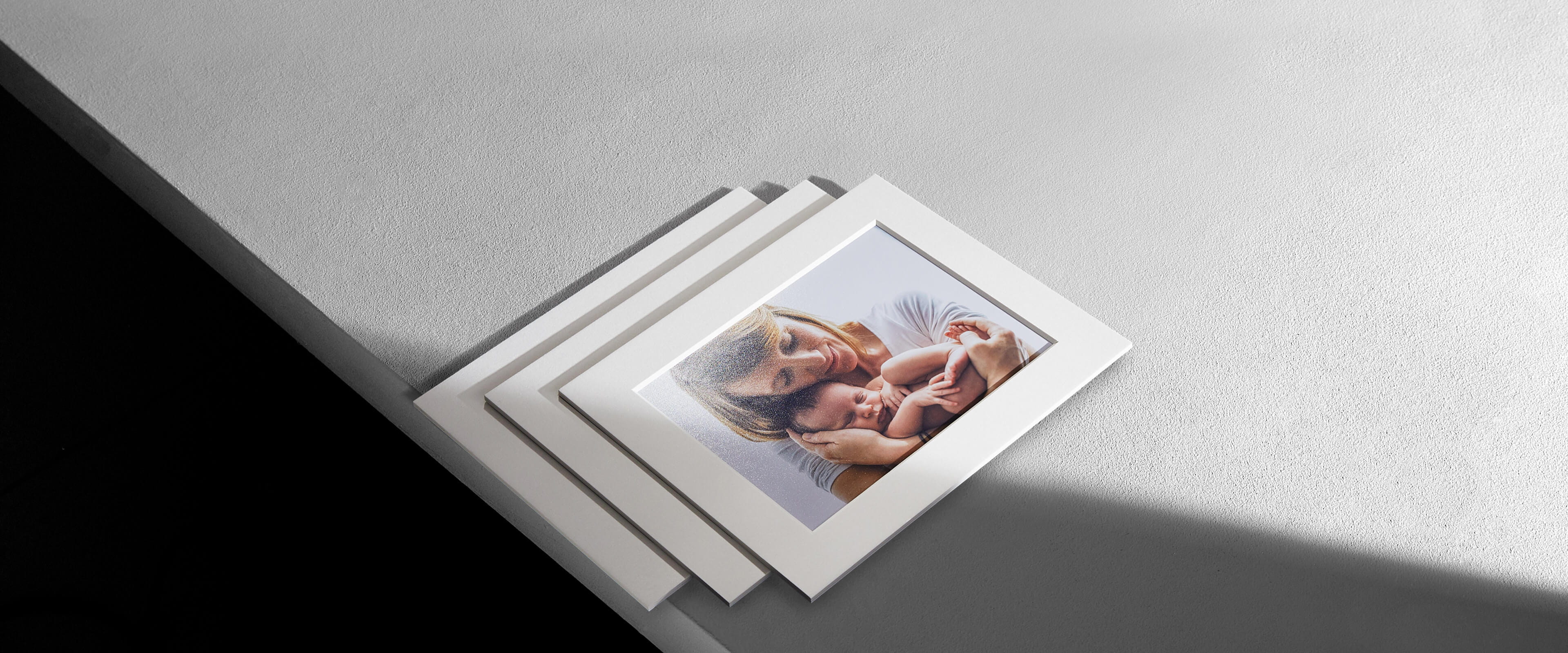 three matted prints on a white table showing a mother holding a baby
